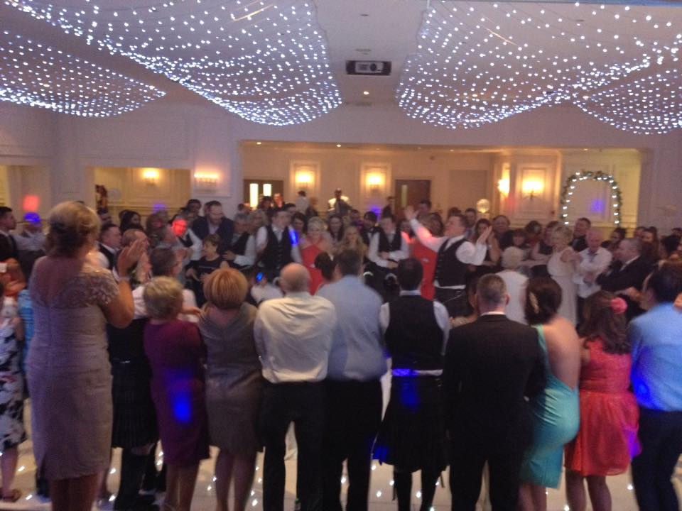 Wedding guests circled around a couple, clapping and singing under fairy-light drapes