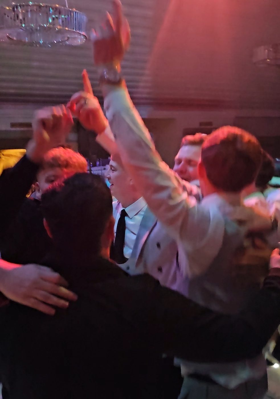 Wedding guests with arms in the air singing along on a warmly lit dancefloor