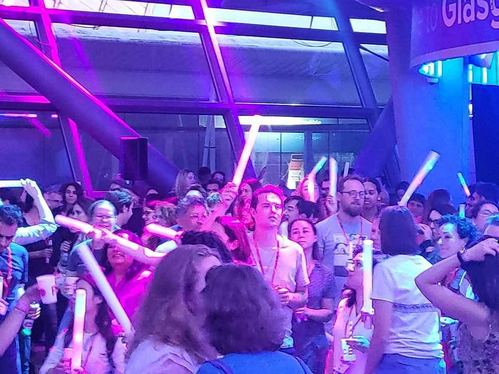 Large crowd of guests waving glowing LED foam sticks under pink and blue lighting at an evening event